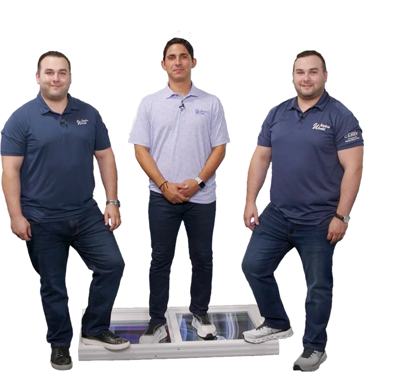 Three men in polo shirts and jeans, two on either side of a white window frame and one standing on it